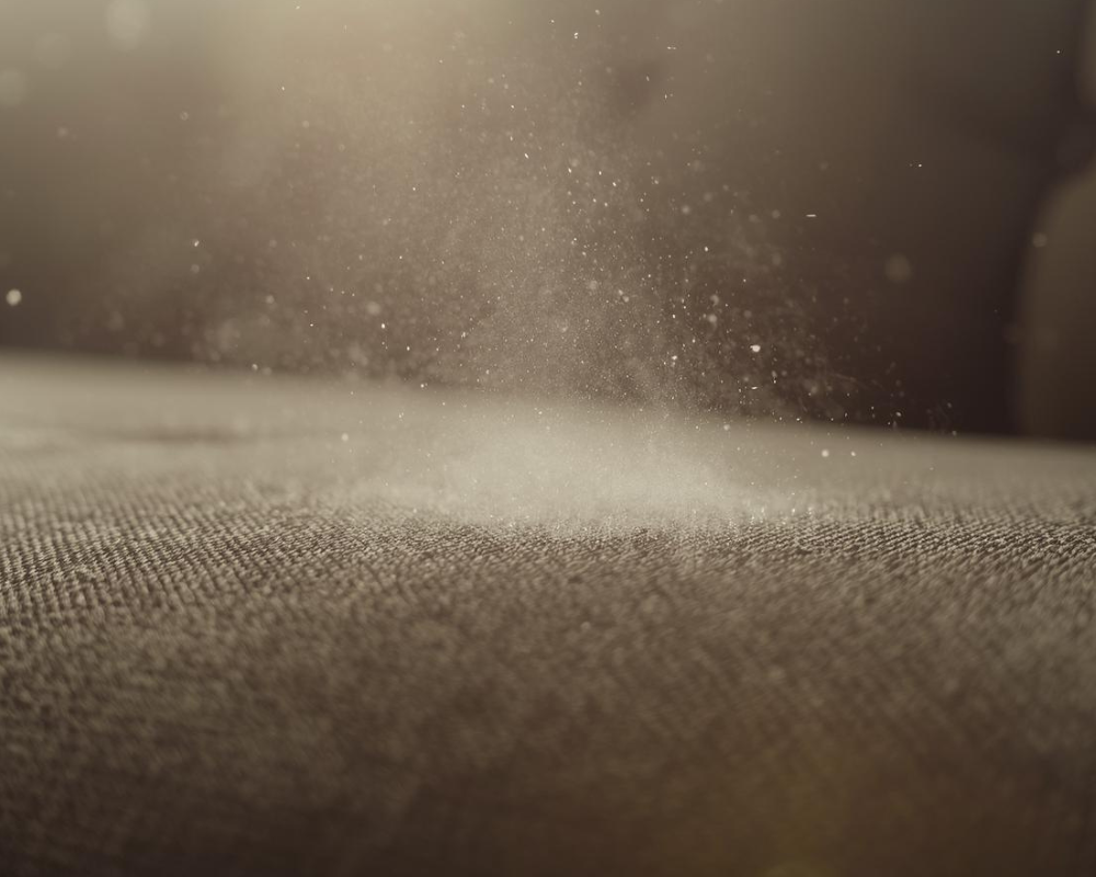 Particules de poussière sur un tissu, symbole de la pollution intérieure et des acariens à éliminer naturellement – Maison Max Clean.