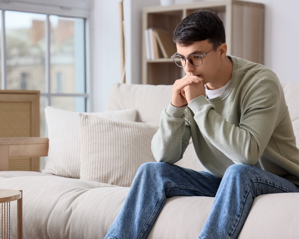 Homme pensif devant un canapé d’occasion dans un salon lumineux à Aix Marseille, questionnement sur le nettoyage canapé occasion – Maison Max Clean Les astuces de Max région PACA