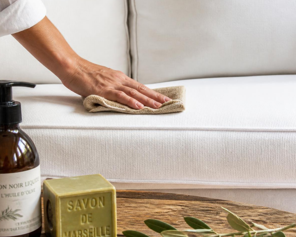 Nettoyage naturel d'un canapé clair avec un chiffon et du savon de Marseille, Les Astuces de Max par Maison Max Clean, spécialiste du nettoyage de canapés à Aix-en-Provence, Marseille et PACA.